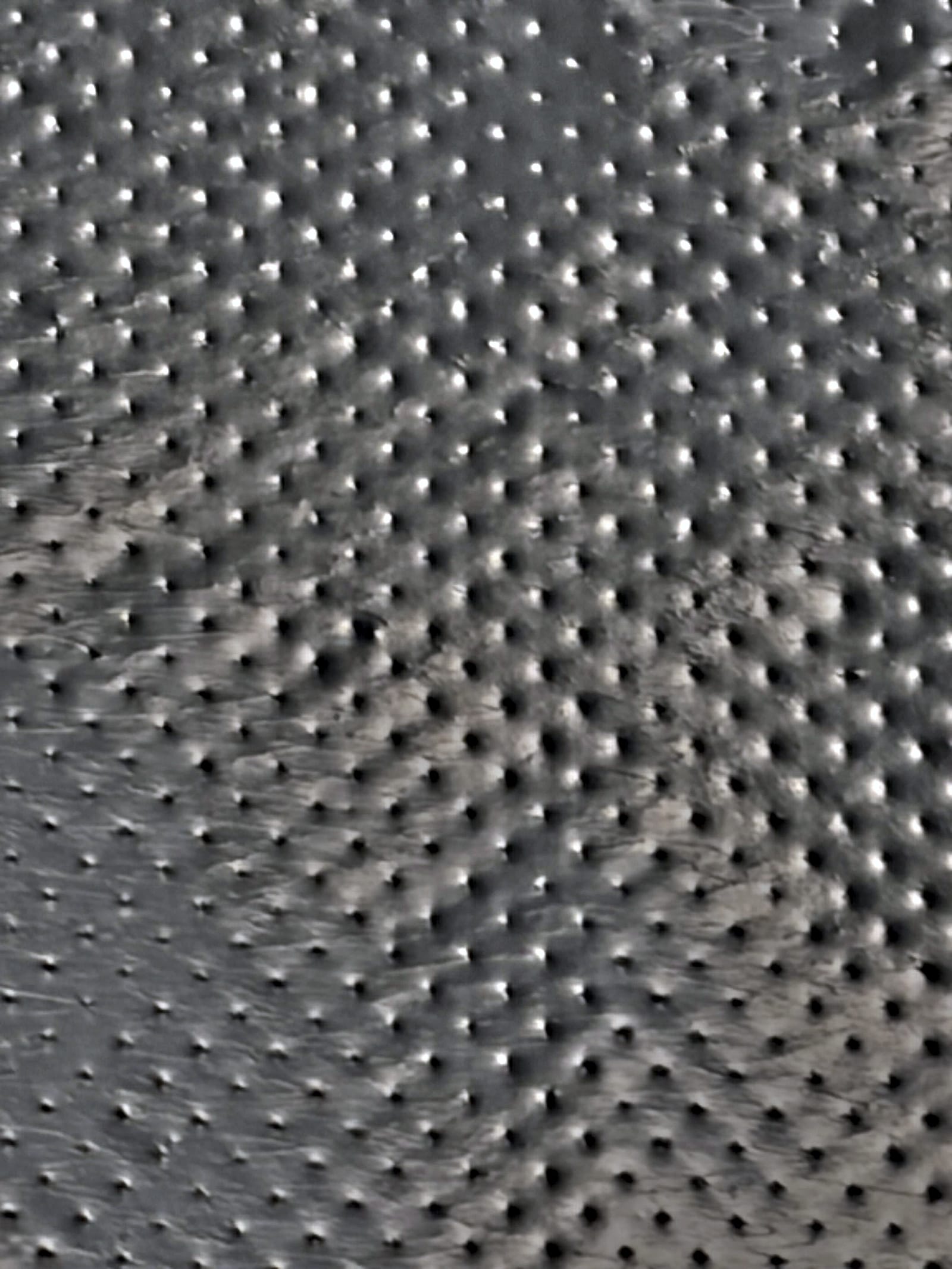 Macro of the embossed dot pattern across the mailer's outer film — the raised points that give an inclined conveyor belt something to grip